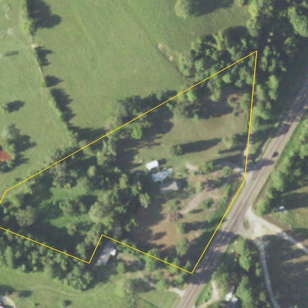 The lot from the air in 2022: a home among trees beside Highway 7, the lot outlined in yellow